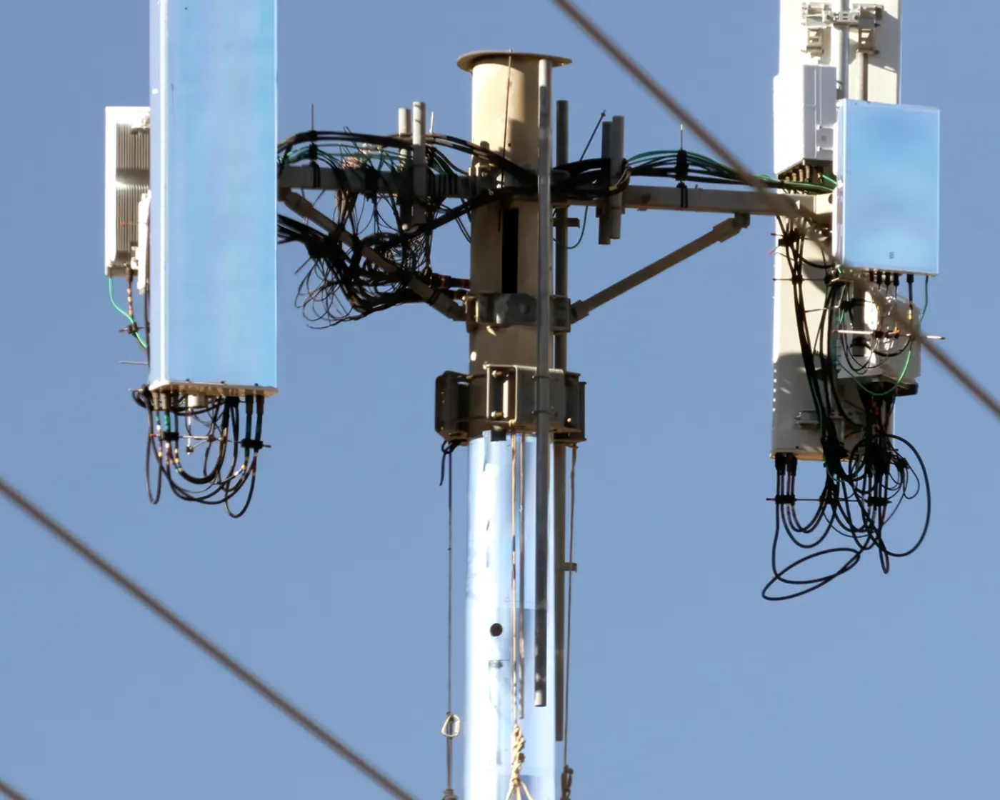 A pole fitted with radio units and cables against a blue sky.